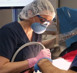 Dental Sterilization Techniques at Pi Dental Center. Photo of a dental assistant suctioning during a dental procedure.